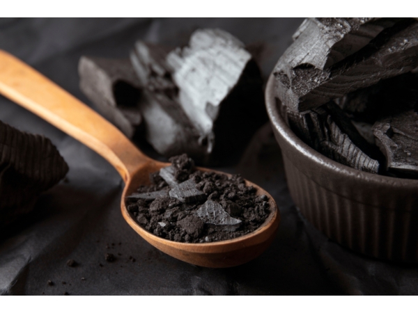 Shilajit darabok és por fakanálban, sötét tál mellett, természetes eredetű étrend-kiegészítőket bemutató blogcikk illusztrációjaként.